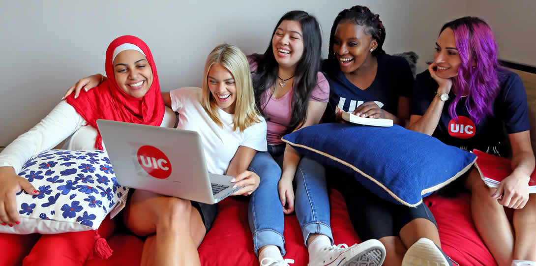 Group of students wearing UIC shirts, using UIC branded laptop, laughing and smiling.